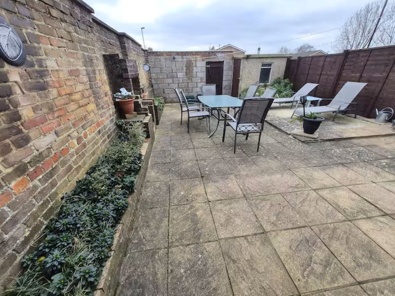 Outdoor patio area with dining table, chairs, loungers and brick walls