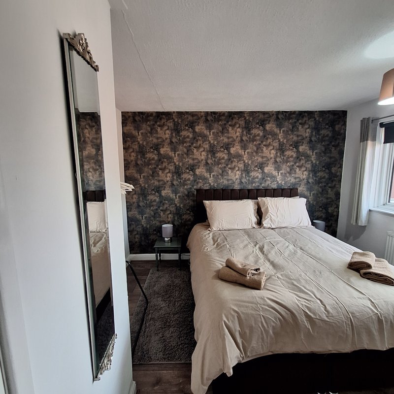 Bedroom with double bed, floral wallpaper accent wall, bedside table and window.