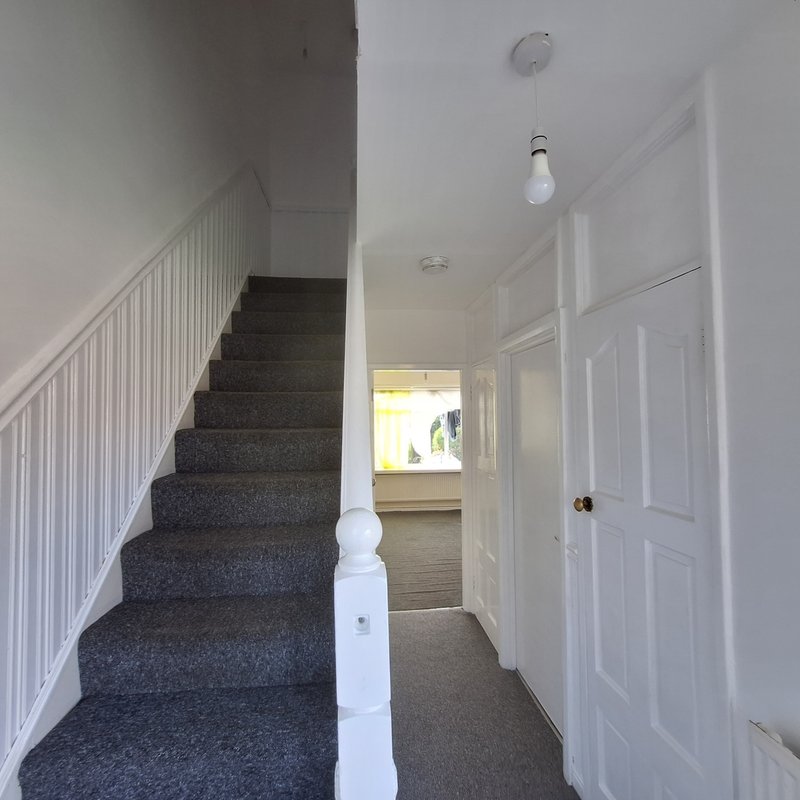Hallway with dark carpeted staircase, white railing, white doors and pendant light fixture
