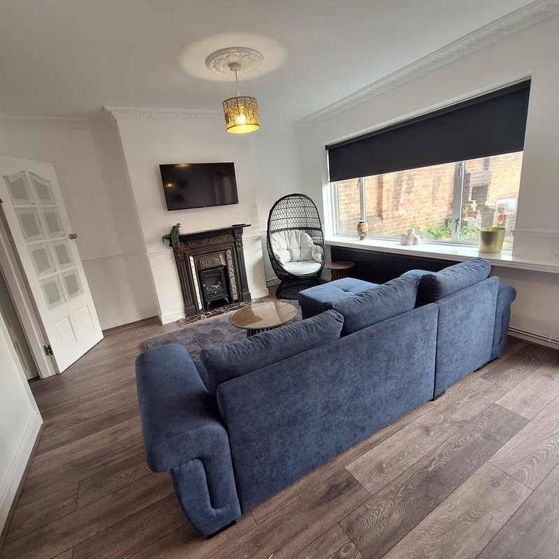 Living room with blue corner sofa, fireplace, wall-mounted TV, and hanging chair by window