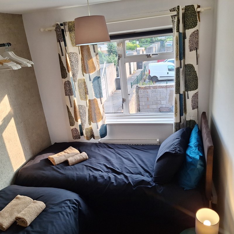 Bedroom with double bed, patterned curtains, window view, and bedside lamp