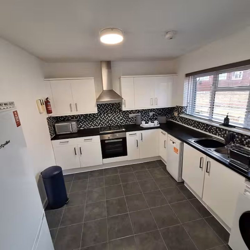 Modern kitchen with white cabinetry, black mosaic tile backsplash, and dark grey floor tiles.