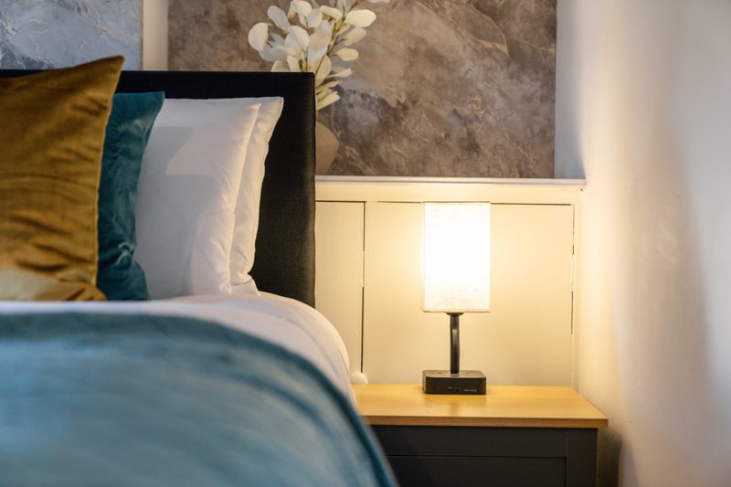 Modern bedroom with blue bedding, decorative pillows, bedside lamp and cream headboard