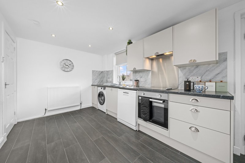 Modern kitchen with white cabinetry, dark grey flooring, stainless steel appliances and marble backsplash