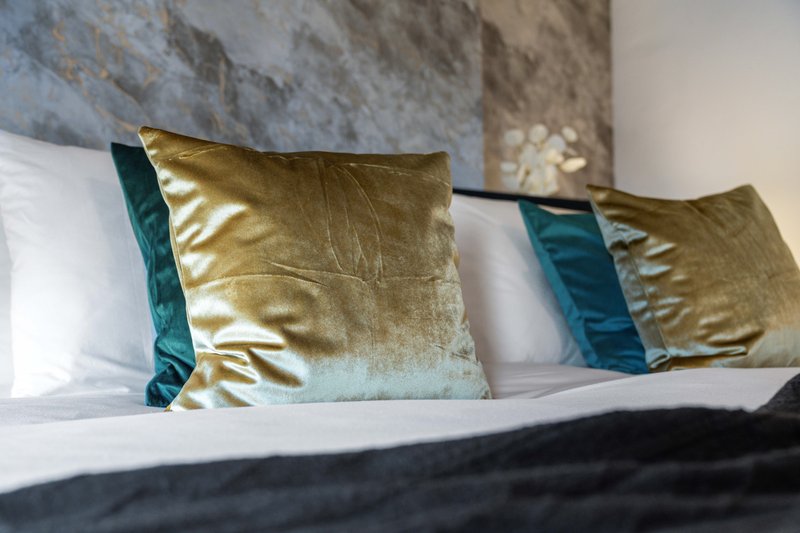 Bed with white pillows and gold and teal decorative cushions against textured wall