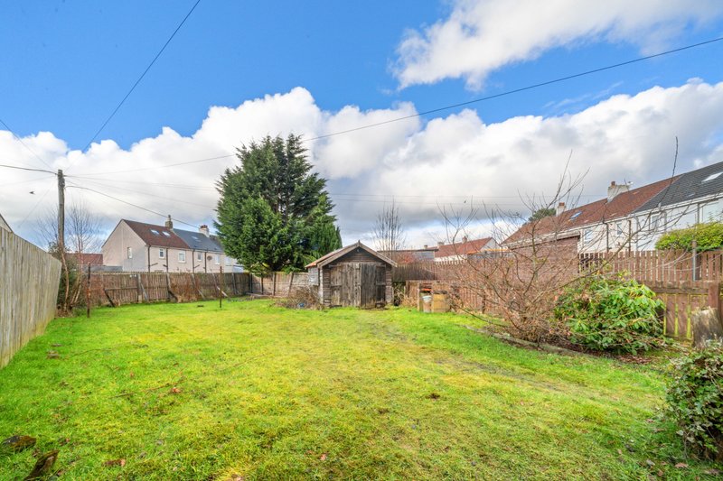Garden with green lawn, wooden fences, shed, and neighbouring houses visible