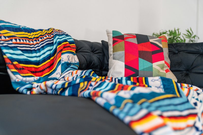 Black sofa with colorful patterned cushions, throws, and blankets arranged on the seating