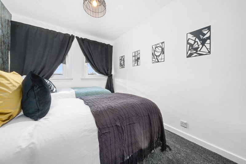 Bright bedroom with double bed, dark bedding, yellow and navy cushions, pendant light fixture