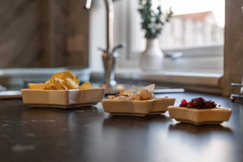 Dark kitchen counter with snacks in wooden bowls, window and potted plant behind