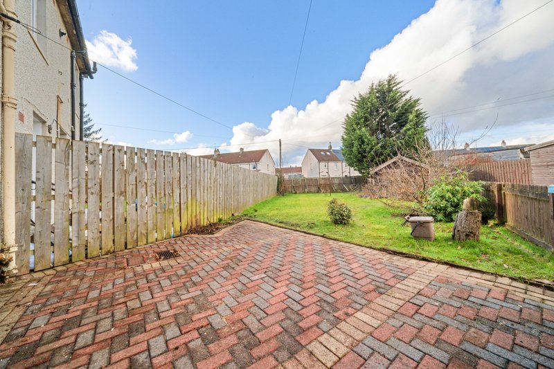 Brick paved garden with wooden fence, lawn area, and neighbouring properties visible