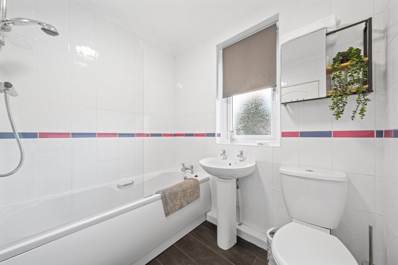 Modern bathroom with white tiles, bath, pedestal sink, toilet and window with plant