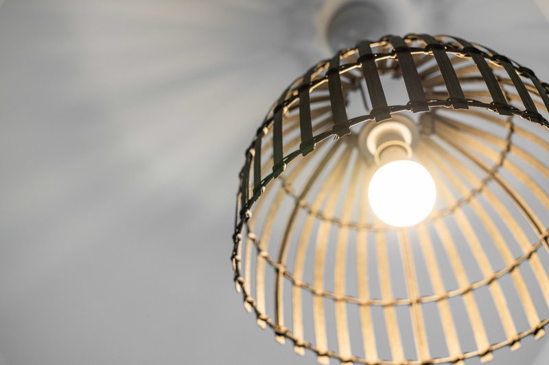 Pendant lamp with black cage shade and illuminated bulb against white ceiling