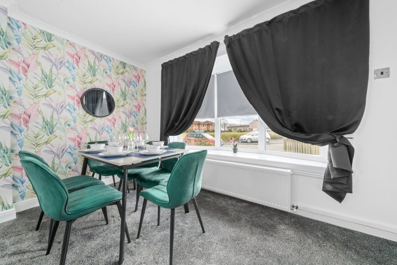 Modern home office with floral wallpaper, green chairs, desk, and large windows with black curtains