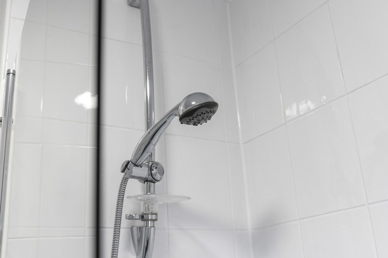 Modern bathroom shower with chrome showerhead and controls on white tiled wall
