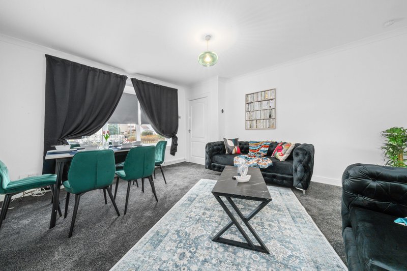Open-plan living and dining area with teal chairs, black sofa, coffee table and window view