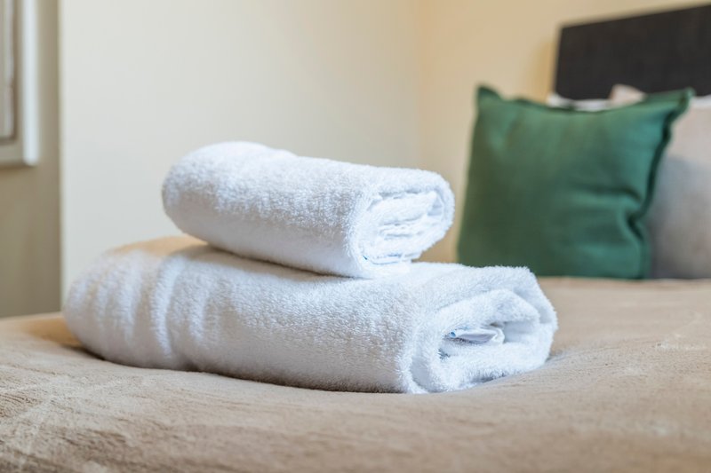 Two rolled white towels on a bed with green cushion and headboard