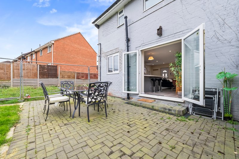 Patio area with black metal chairs and table, adjacent to modern house with glass doors and garden