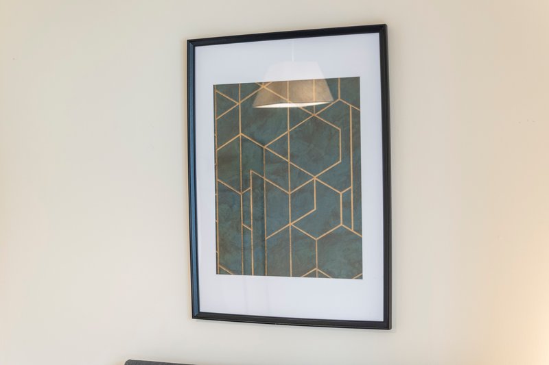 Framed abstract geometric art print with gold lines on teal background hanging on white wall