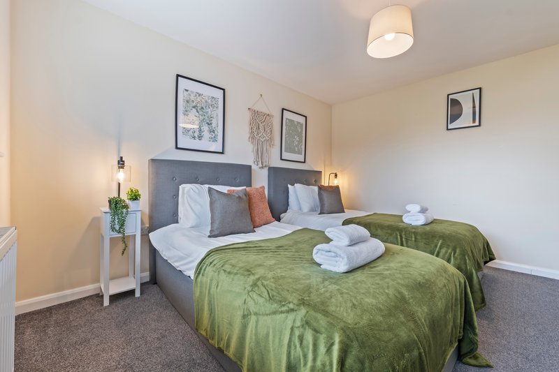 Bright bedroom with twin beds, green bedding, framed wall art, and bedside lamps