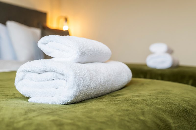 Rolled white towels on green bedspread in modern bedroom with headboard