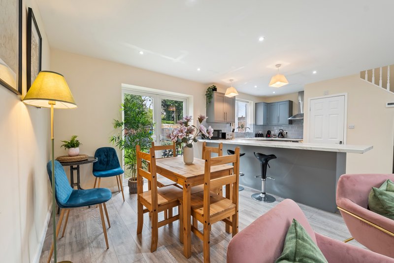 Open-plan living and dining area with wooden table, blue chairs, pink sofa, and modern kitchen
