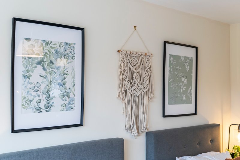 Bedroom wall with framed botanical prints, macramé wall hanging, and upholstered headboard