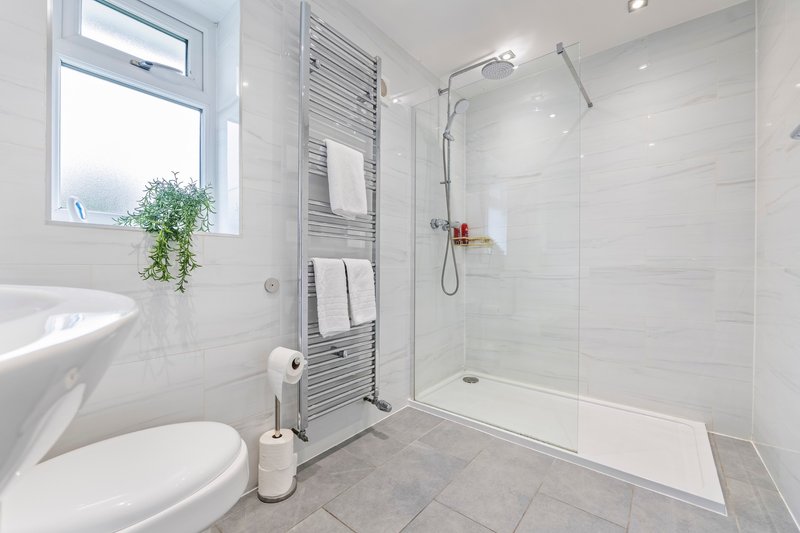Modern bathroom with white tiles, walk-in shower, toilet, heated towel rail and window
