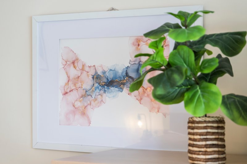 Wall art with abstract watercolor design, potted plant with green foliage in woven pot