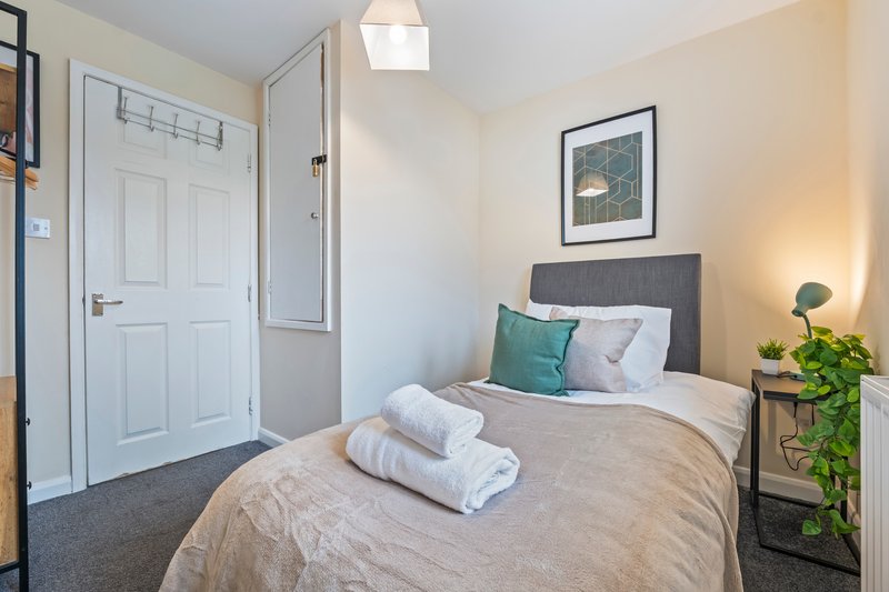 Bright bedroom with double bed, rolled towels, bedside table, plant, and white door