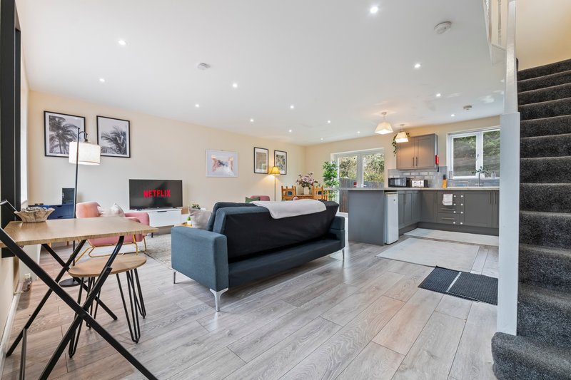 Open-plan living area with blue sofa, work desk, kitchen and stairs visible