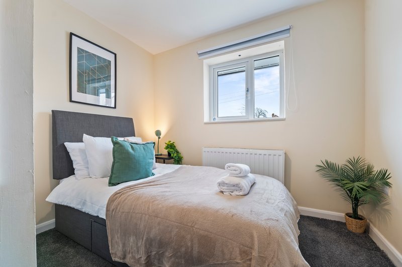 Bright modern bedroom with double bed, grey headboard, white pillows and potted plant by window
