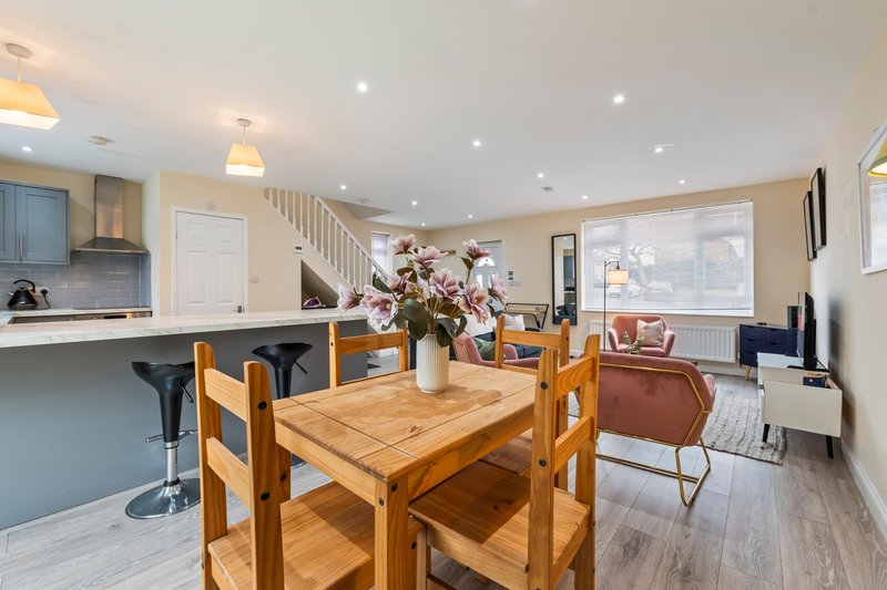 Open-plan kitchen and dining area with wooden table, bar seating, and stairs visible