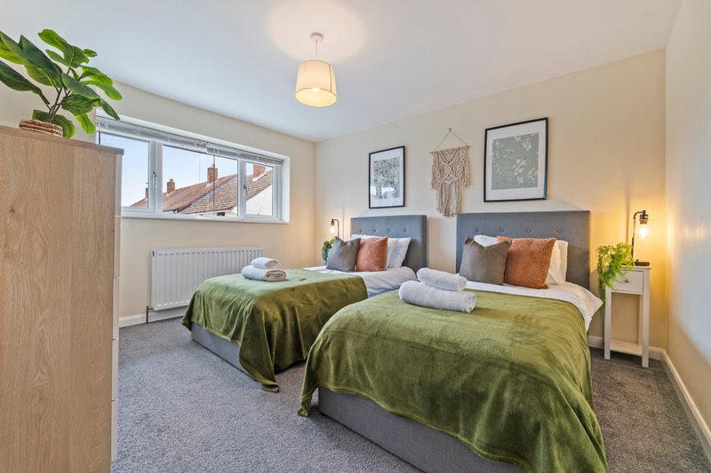 Bright bedroom with two single beds, green bedding, framed wall art and window view