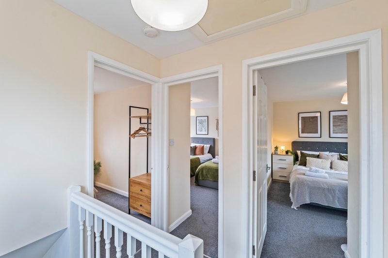 Landing area with white banister overlooking multiple bedrooms with open doors and beds visible