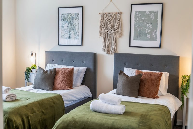 Twin bedroom with two beds, olive green bedding, cushions, framed wall art and macramé décor