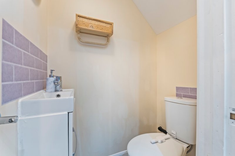 Small bathroom with white toilet, sink, purple tile backsplash and wooden shelf
