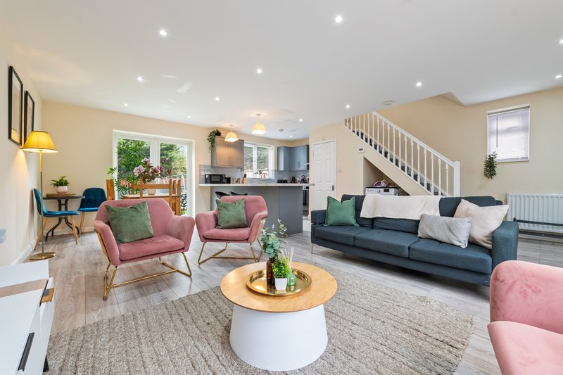 Open-plan living room with pink armchairs, navy sofa, wooden coffee table and stairs