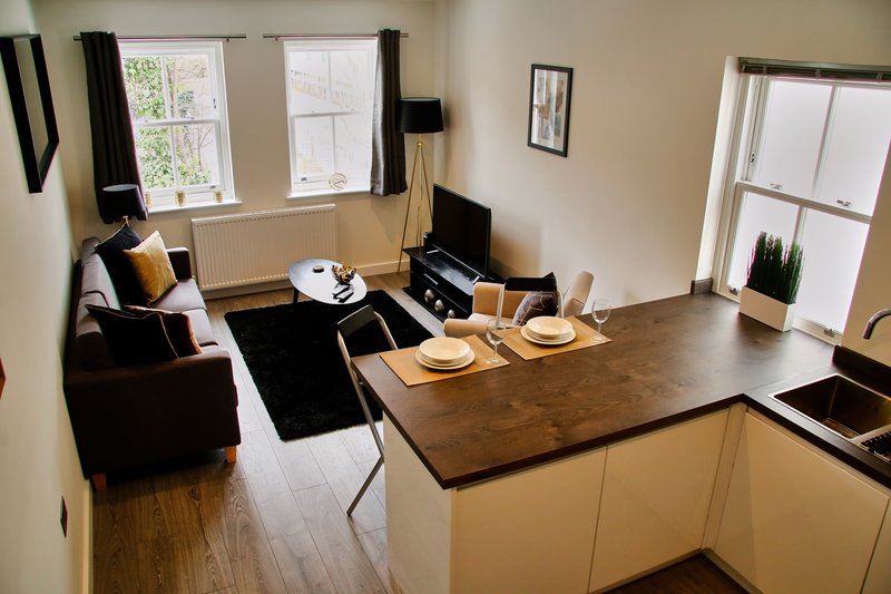 Open-plan living area with kitchen, dining table set for two, and lounge seating by windows