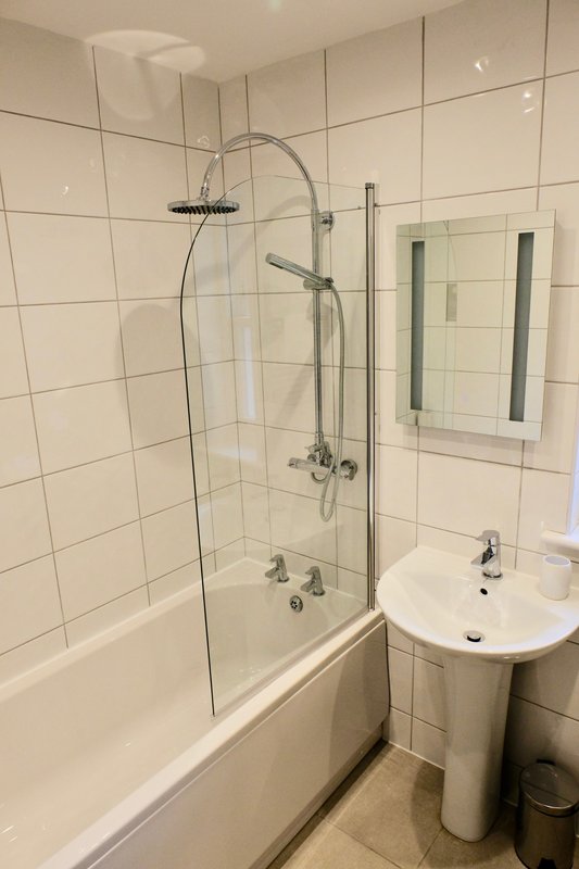 Modern bathroom with white tile walls, glass shower enclosure, bathtub and pedestal sink