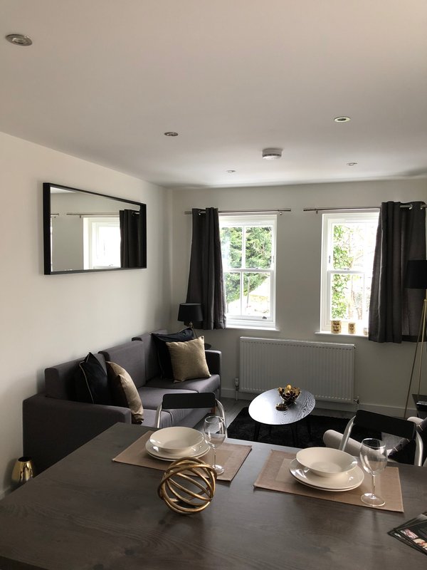 Open-plan living and dining area with black sofa, dining table, mirror and windows