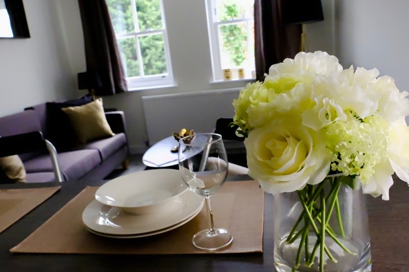 Dining table with place settings and yellow flower arrangement, living area with sofa visible
