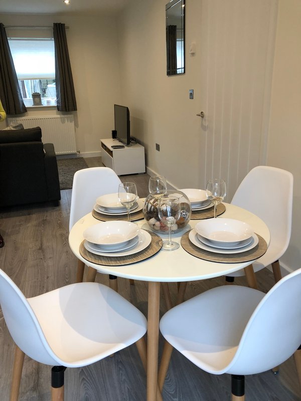 Dining area with round table, four white chairs, place settings and water pitcher
