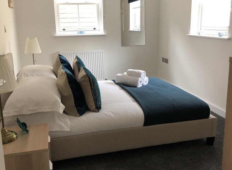 Bright bedroom with made bed, decorative pillows, bedside table with lamp and windows