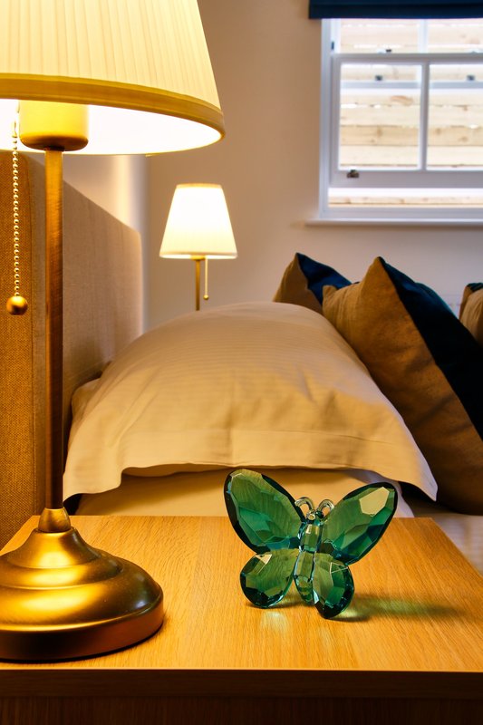 Bedroom with double bed, gold lamps, decorative green butterfly ornament on nightstand