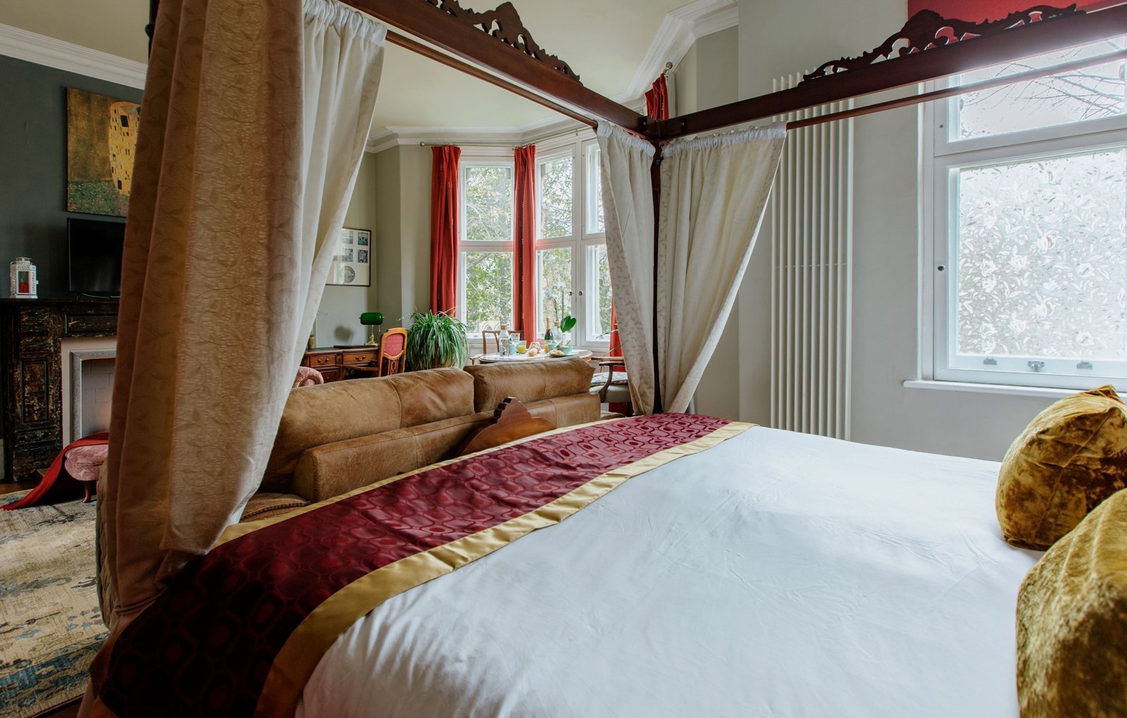 Luxury bedroom with four-poster bed, burgundy runner, cream bedding, and large windows with curtains