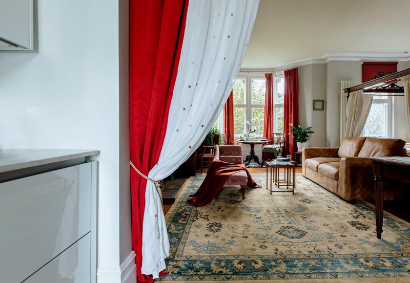 Bright living room with red and white curtains, brown sofa, patterned rug and garden views