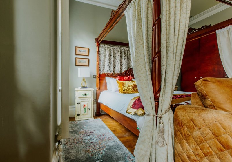 Bedroom with four-poster bed, cream curtains, wooden frame, and decorative pillows
