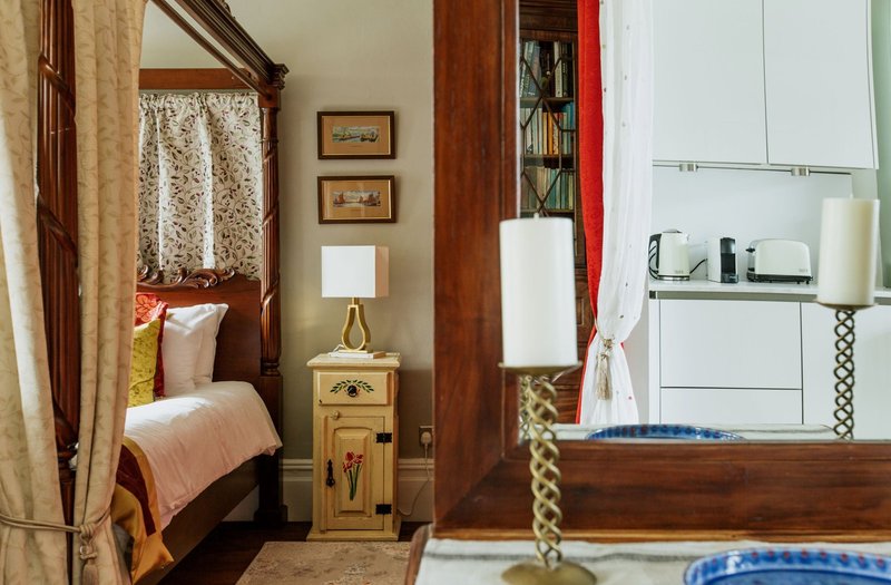 Bedroom with wooden four-poster bed, nightstand, lamp, and ensuite bathroom visible through doorway