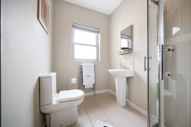 Clean bathroom with toilet, pedestal sink, shower enclosure and window