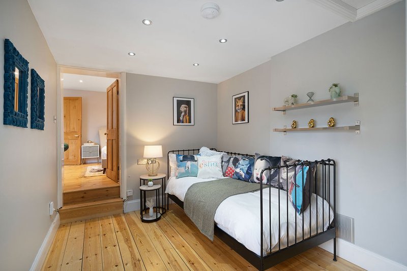 Bedroom with single bed, wooden flooring, wall art, shelving and open doorway to hallway